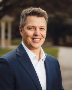 Portrait of Community Foundation president Matt Morton who has light brown hair. He is smiling and wearing a white collared shirt with a blue suit jacket.
