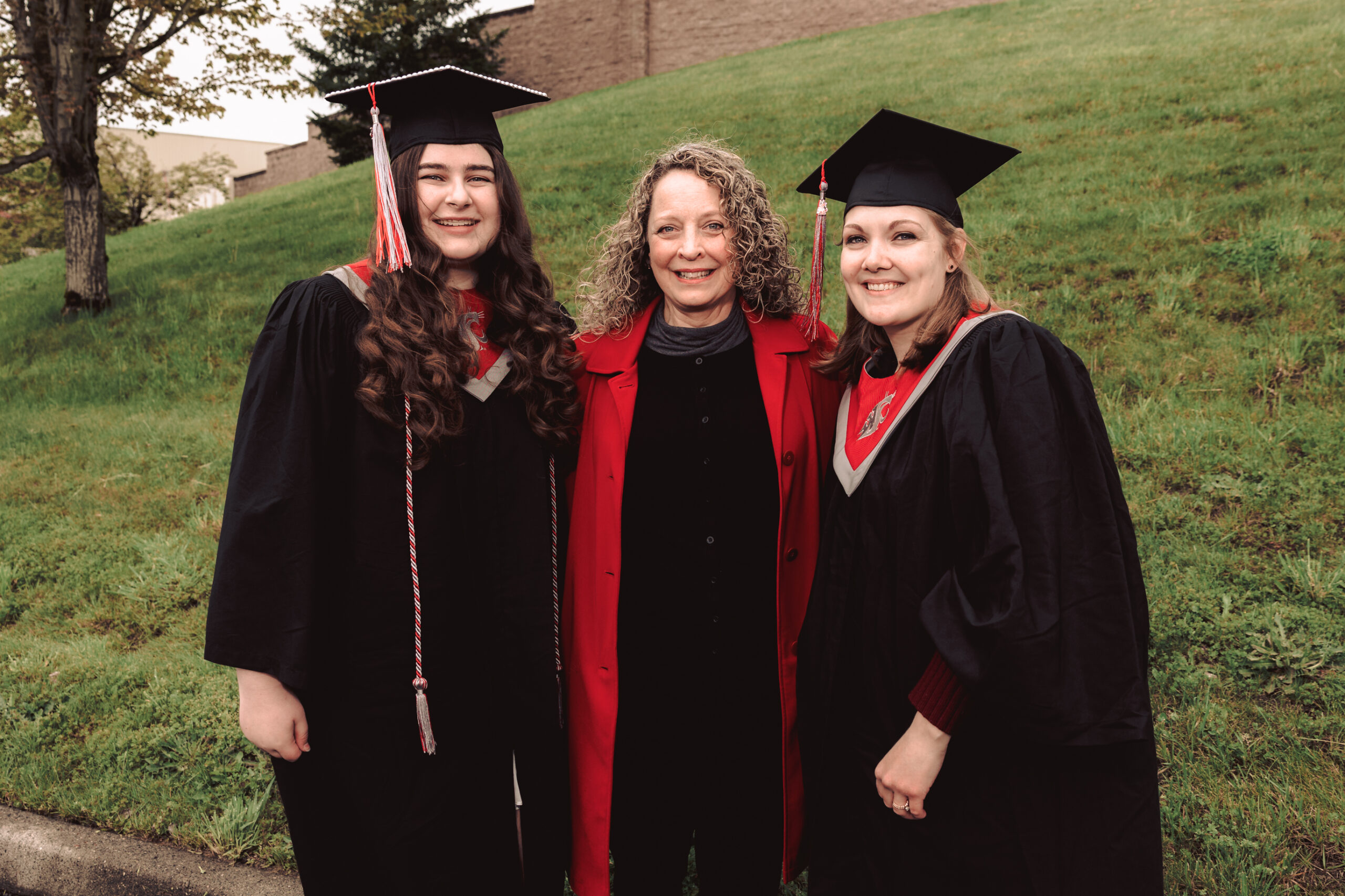 Two Washington State University Vancouver graduates smiling into the camera on graduation day with Deanna Green, scholarship manager, smiling in between them.